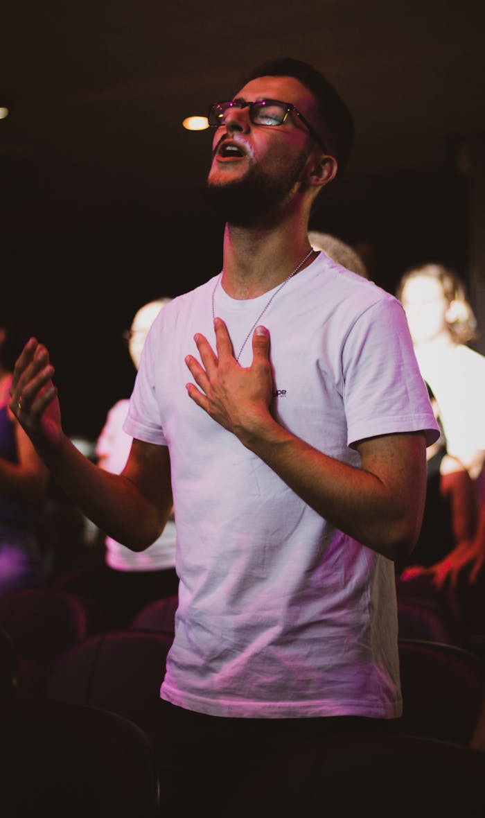 A man in a white shirt praying in a dimly lit worship setting.